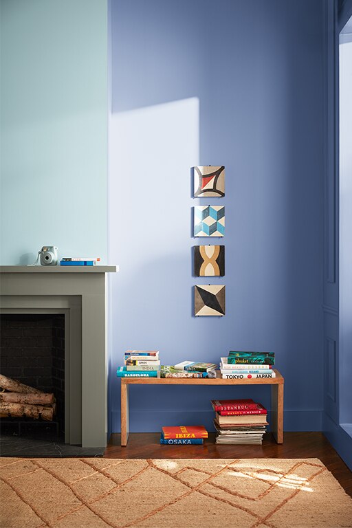 The corner of a living room with a wall painted in Polar Sky 1674, a fireplace painted in Antique Pewter 1560, a orange rug and a book-filled bench