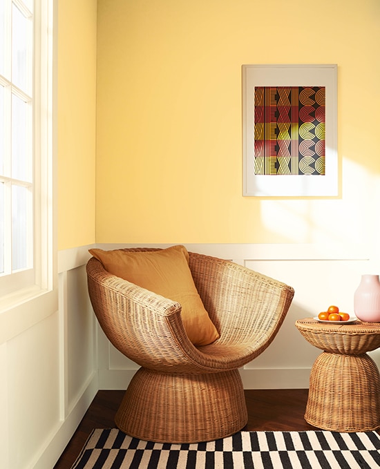 A two-tone room combining Honeybee CSP-950 and White Dove OC-17. Styling features a rattan chair and table, a golden cushion, a modern print and patterned rug