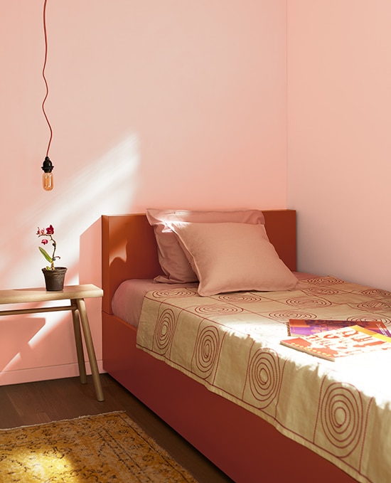 A bedroom decorated with Teacup Rose 2170-50. The bedframe is a burnt orange colour. An decorative bulb pendant lamp hangs from the ceiling over a wooden side table