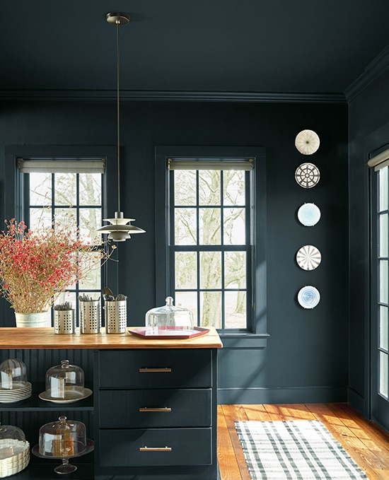 A kitchen colour-drenched in Regent Green 2136-20. It features a wooden floor and worktop with glass cake stands arranged on open shelving and a large flowering plant