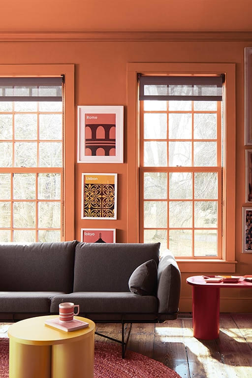 A bold living room with walls and woodwork painted in a deep radiant Topaz 070 with styling featuring wall posters, a dark gray couch and a round yellow coffee table