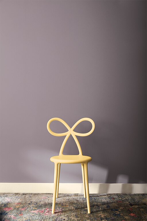 A small chair with bow-shaped back painted in Honeybee CSP-950 in front of a wall painted with Hazy Lilac 2116-40 and skirting boards painted in White Dove OC-17