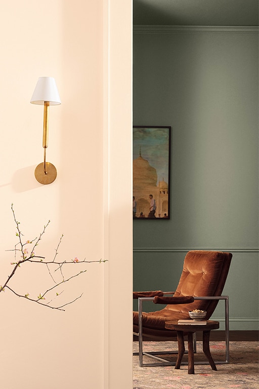 A hallway painted in Pristine OC-75 with a view through to a sitting room painted in Antique Pewter 1560, styled with an upholstered red chair and wooden side table