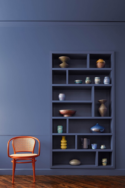 A serene space colour-drenched with Blue Nova 825, featuring built-in shelving adorned with decorative vases and a small leather club chair