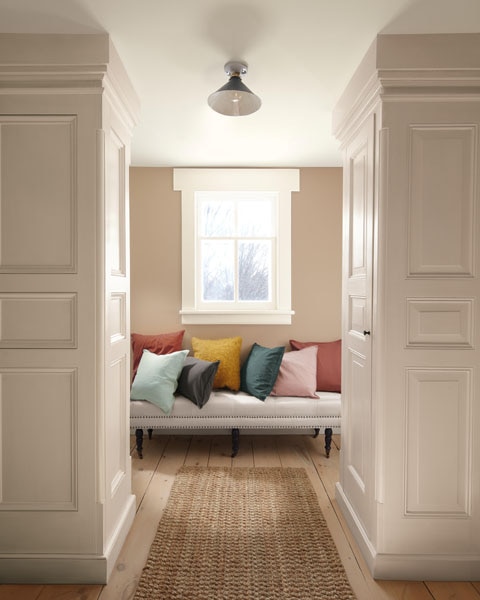 A vignette featuring a contemporary bench with colourful cushions. The walls are painted in Sherwood Tan 1054 and the panelling is painted in First Crush CSP-310.