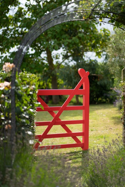 A garden gate painted in Ruby Red 2001-10, Aura Exterior Satin, surrounded by lush foliage