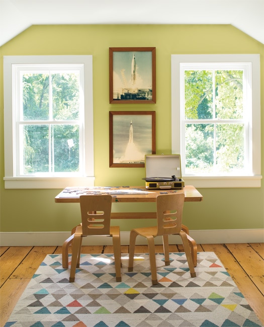 A contemporary study with walls painted in Green Hydrangea CSP-850. A colourful triangle-patterned rug and desk with 2 chairs, styled with a puzzle and record player, complete the look