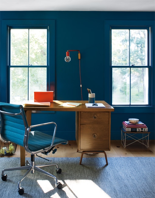 A colour drenched space with walls, window frames and skirting boards all painted in Hidden Sapphire CSP-690.  The room is styled with wooden writing desk,  blue desk chair and vibrant orange wall light